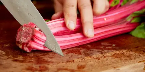 Eine Hand schneidet mit einem Messer die roten Stiele von Mangold. Die Zubereitung von Mangold Stiele beginnt.