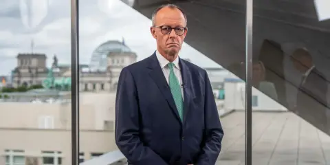 Mann im Anzug blickt nachdenklich, während im Hintergrund das Reichstagsgebäude zu sehen ist. Er spricht über die **Herausforderungen des Sozialstaats**.
