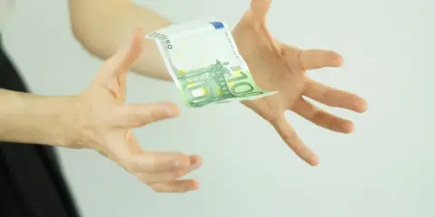 Hände fangen einen 100-Euro-Schein, der schwebt. Ein Symbol für ein Leben ohne Geld, das vielleicht doch möglich ist.