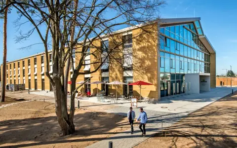 Modernes Gebäude mit Glasfront und Fassade aus nachhaltigen Materialien. Zwei Männer gehen auf einem Weg.