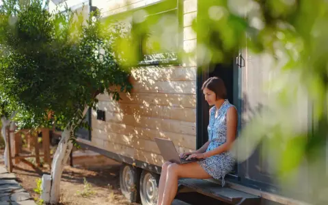 Frau arbeitet auf Laptop vor einem Tiny House. Ein Beispiel für modernes, flexibles wohnen in der zukunft.