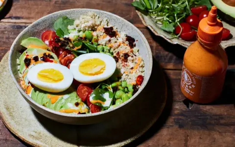 Gesunde Bowl-Ideen: Quinoa, Avocado, Ei, Edamame und Kirschtomaten, beträufelt mit Sriracha-Mayo.