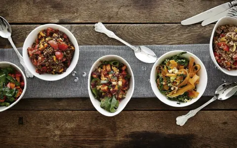 Verschiedene Salate als Beilagen für ein Fondue: Linsensalat, Gemüsesalat mit Karotten und Grünkohl, sowie ein weiterer bunter Salat.