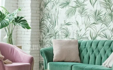 Ein grünes Samtsofa und ein rosafarbener Sessel mit einer Monstera-Pflanze. Die Wand hinter dem Sofa ist mit einer tropischen Tapete mit Palmenblättern dekoriert, eine tolle Idee, um zwei Tapeten zu kombinieren.