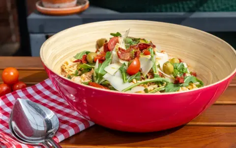 Leckere nudelsalat ideen: Pasta mit Rucola, Tomaten, Oliven und Parmesan in einer roten Schüssel.