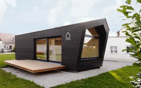 Modernes, dunkles Cabin House mit Holzterrasse und großem Fenster. Ein stilvolles Zuhause für minimalistisches Wohnen.