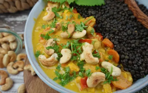 Ein cremiges Beluga Linsen Curry mit Cashewkernen und frischer Petersilie, daneben eine Portion schwarzer Beluga Linsen.
