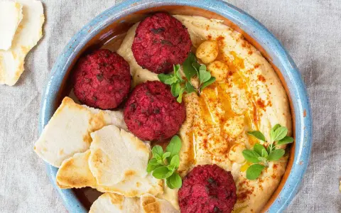 Rote Bete Falafel auf cremigem Hummus, garniert mit Kichererbsen und frischen Kräutern, serviert mit Pitabrot.