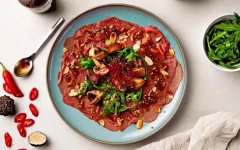 Rindercarpaccio mit Pilzen, Rucola und Mandeln. Eine köstliche Variation von Carpaccio, garniert mit Chili und Trüffel.