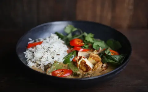 Schüssel mit Reis und einem köstlichen rotes thai curry mit Tofu, Chili und frischen Kräutern.
