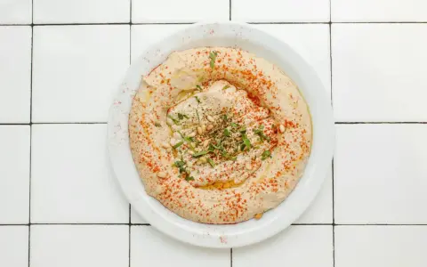 Cremiger Hummus-Dip mit Paprikapulver, Pinienkernen und Petersilie auf einem Teller, bereit zum Dippen.