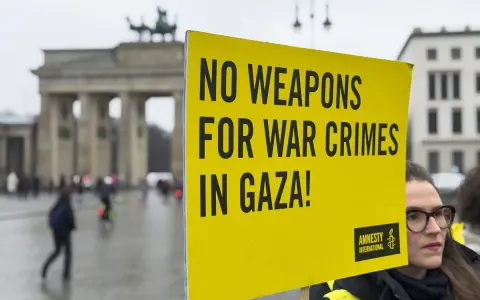 Gelbe Tafel mit Aufschrift "NO WEAPONS FOR WAR CRIMES IN GAZA!" vor dem Brandenburger Tor. Amnesty International setzt sich für Menschenrechte ein.