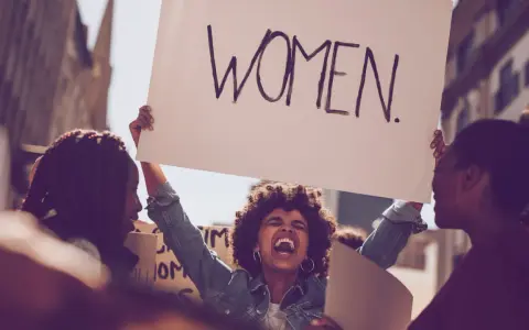 Frauen demonstrieren für Gleichberechtigung. Eine Frau hält ein Schild mit der Aufschrift "WOMEN". Das zeigt, was feminist ist: eine Stimme für Frauen.