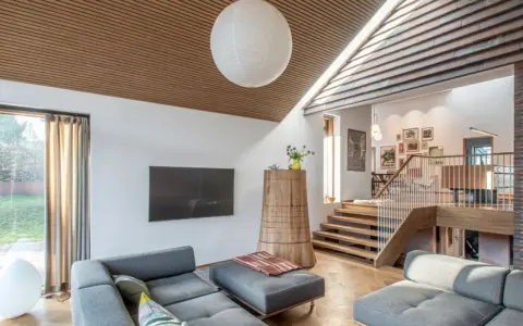 Modernes Wohnzimmer mit grauem Sofa und einem interessanten **split level** Design, das durch eine Holztreppe und einen offenen Wohnbereich gekennzeichnet ist.