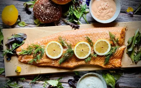 Flammlachs mit Zitronenscheiben und Dill, serviert mit cremigen Dips und frischem Salat als Beilagen.
