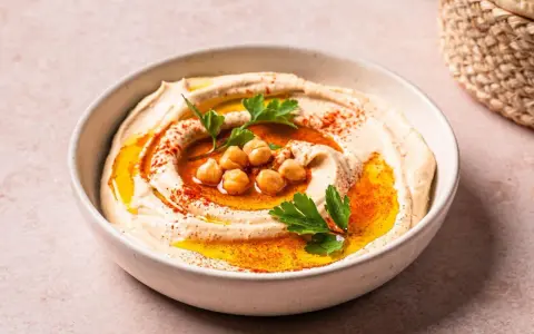 Cremiger Hummus in einer Schüssel, garniert mit Kichererbsen, Petersilie und Paprikapulver. Ein köstliches Gericht mit Hummus, bereit zum Genießen.