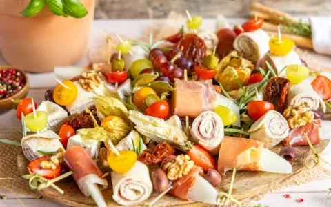 Bunte Platte mit Fingerfood-Dips: Prosciutto-Röllchen, Käse, Trauben, Tomaten, Physalis und Nüsse. Perfekt für jede Party!