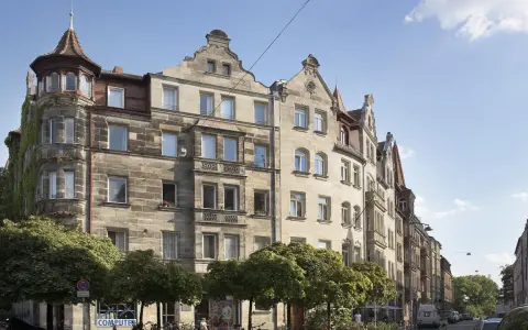 Ein prächtiges Jugendstil Haus mit Erker und Türmchen, umgeben von Bäumen, steht an einer belebten Straße.