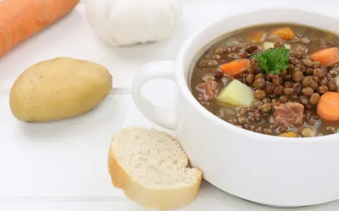 Herzhafte Linsensuppe nach DDR-Rezept mit Kartoffeln, Karotten und Speck. Dazu ein Stück Brot.