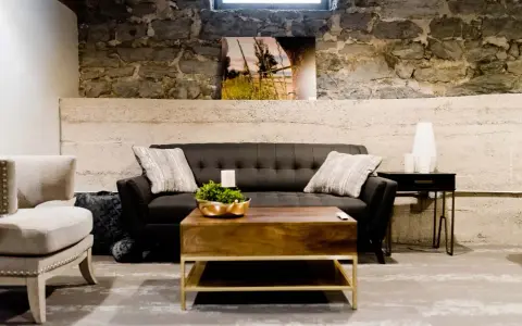 Gemütliches Wohnzimmer im industrial style mit dunklem Sofa, Holztisch und Steinwand.
