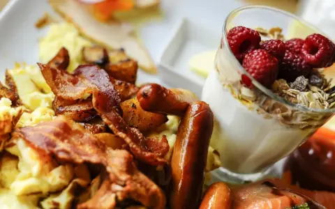 Herzhafte Ideen zum Brunch: Rührei, Speck, Würstchen und Kartoffeln neben einem Glas Joghurt mit Beeren und Müsli.