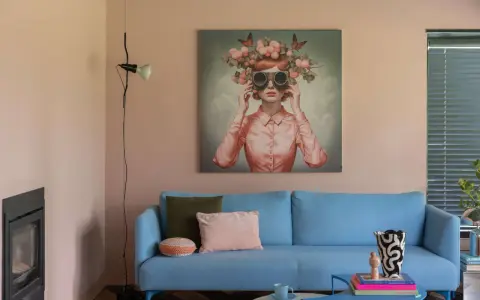 Ein hellblaues Sofa mit Kissen vor einem Bild, das eine Frau mit Blumenkranz und Schmetterlingen zeigt. Ein Beispiel für die Wohntrends 2026.