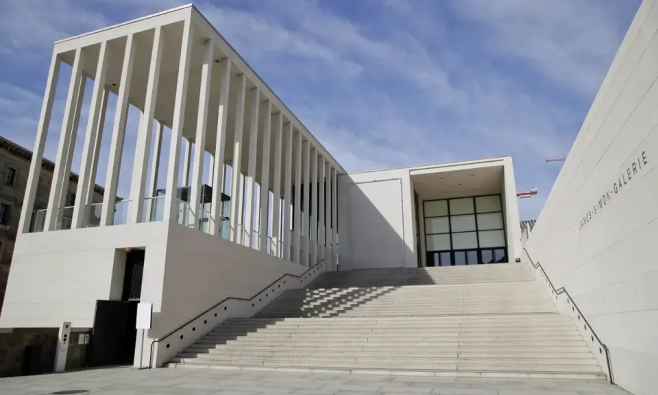 Moderne James-Simon-Galerie mit langer Treppe, ein Werk bekannter Architekten, vor blauem Himmel.