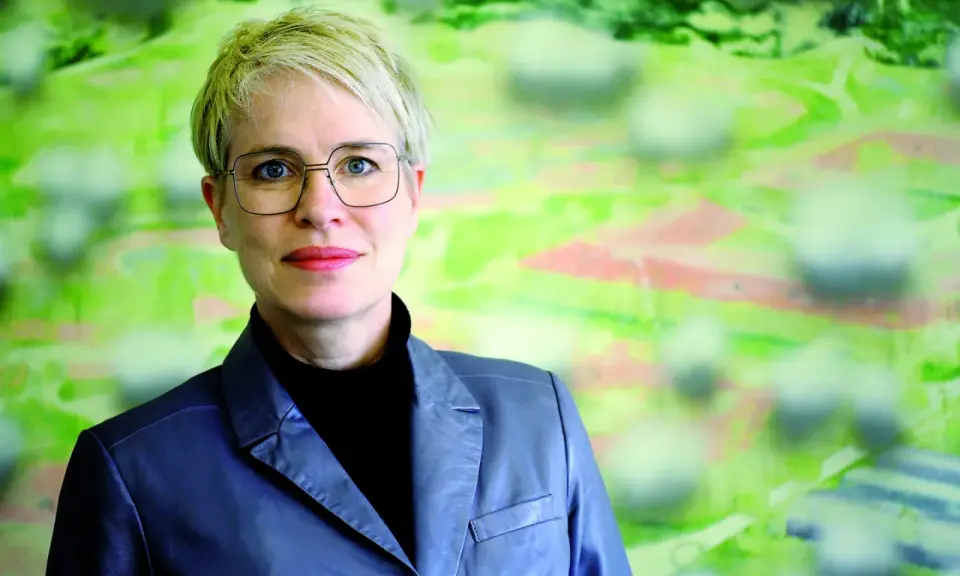Frauke Burgdorff, eine Frau mit kurzen blonden Haaren und Brille, blickt lächelnd in die Kamera. Sie trägt einen grauen Blazer.