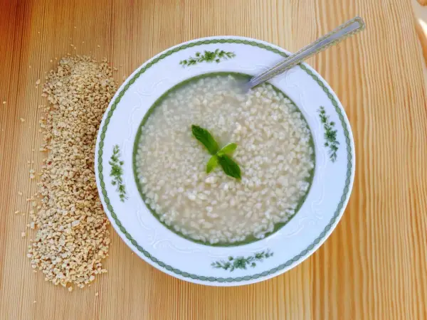 Eine Schüssel mit Trahana, garniert mit Minze, neben einem Haufen getrockneter Trahana. Ein Löffel liegt in der Schüssel.