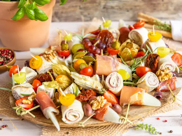 Bunte Platte mit Fingerfood-Dips: Prosciutto-Röllchen, Käse, Trauben, Tomaten, Physalis und Nüsse. Perfekt für jede Party!